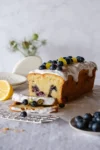 Blaubeerkuchen mit Royal Icing: Auf dem Foto ist neben dem angeschnittenen Kuchen mit Heidelbeeren und Zitronenzesten auf dem Guss noch eine angeschnittene Zitrone zu sehen.