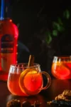 Zwei Gläser mit Hot Aperol alkoholfrei und einer Orangenscheibe, daneben Spekulatius und eine Flasche Bitter Sirup.