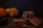 Ein Stapel mit Kürbis Brownies und Schokoguss, im Hintergrund Kürbisse