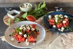 Zwei Teller mit dem fertig angerichteten Wassermelonen-Feta-Salat mit Rucola